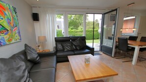 A modern living room with a black leather sofa, a wooden coffee table, and a dining area with a table and chairs. - Schmalstieg 11 a, Wyker Perle - Holiday home with 3 rooms on approx. 81m² (Wyk auf Föhr)