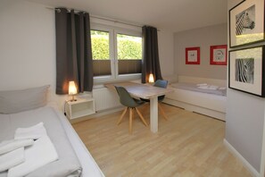 Quarto com cama, escrivaninha, cadeira, sofá e janela com cortinas.