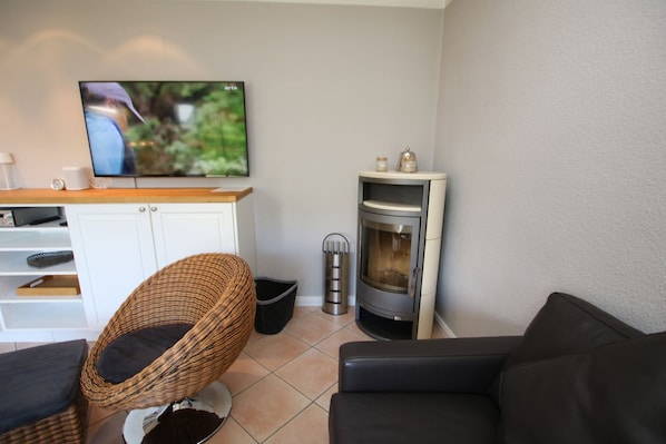 A living room with a television, a fireplace, a wicker chair, a black sofa, and a white cabinet.