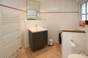 Ein Badezimmer mit Waschbecken, Spiegel, Toilette und Waschmaschine.