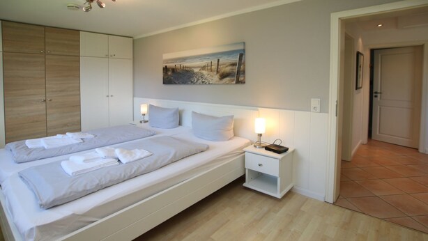 A bedroom with a large bed, bedside tables, a wardrobe, and a painting on the wall. - Schmalstieg 11 a, Wyker Perle - Holiday home with 3 rooms on approx. 81m² (Wyk auf Föhr)
