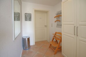 A hallway with a door, a trash can, a chair, and a rack with hangers.
