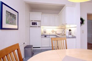 A compact kitchen with white cabinetry, a microwave, and a sink. There is a dining table with chairs in the foreground.