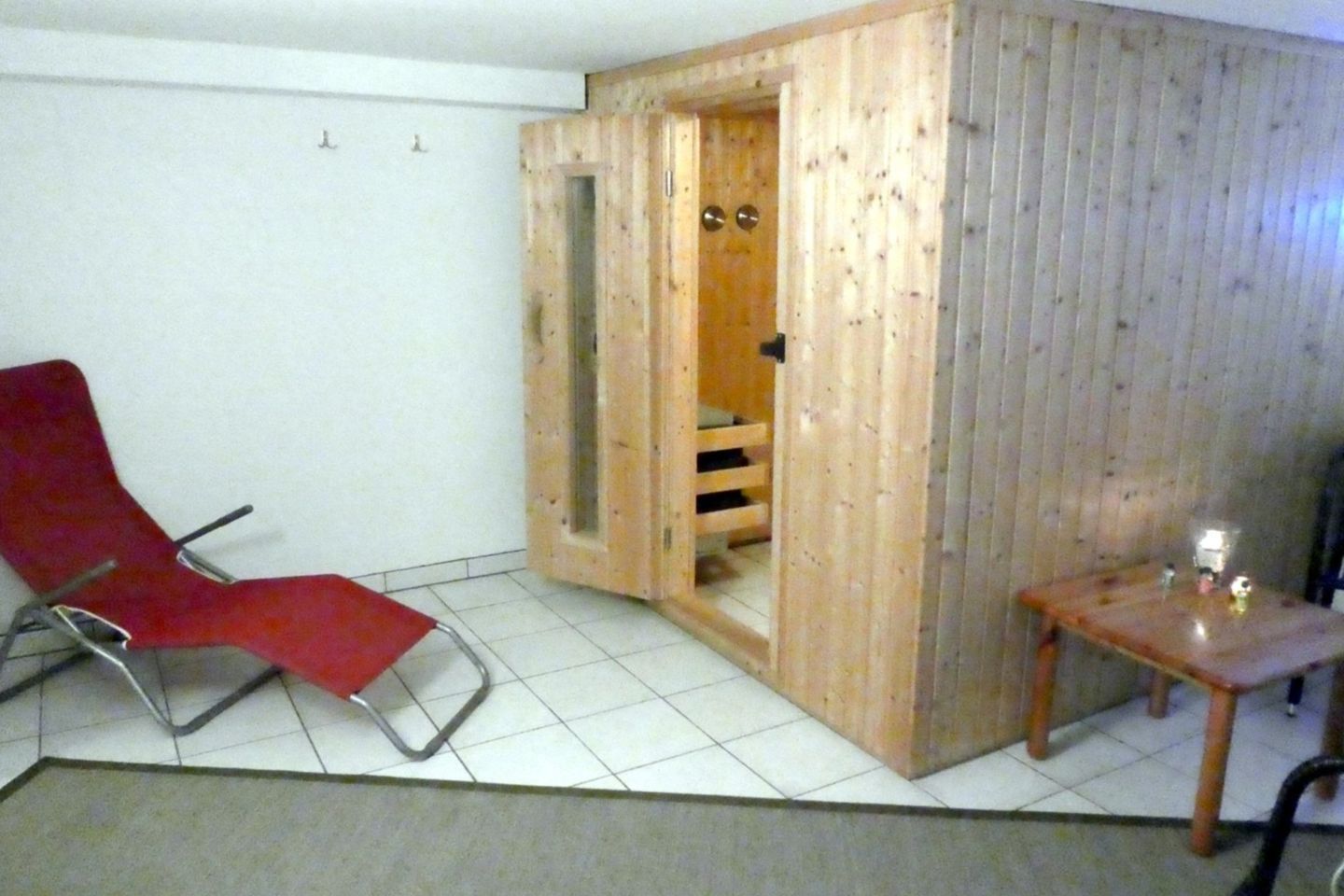Une pièce avec une chaise rouge, une porte en bois et une petite table sur laquelle se trouve une bougie.
