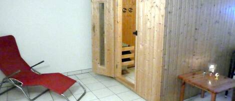 Une pièce avec une chaise rouge, une porte en bois et une petite table sur laquelle se trouve une bougie.