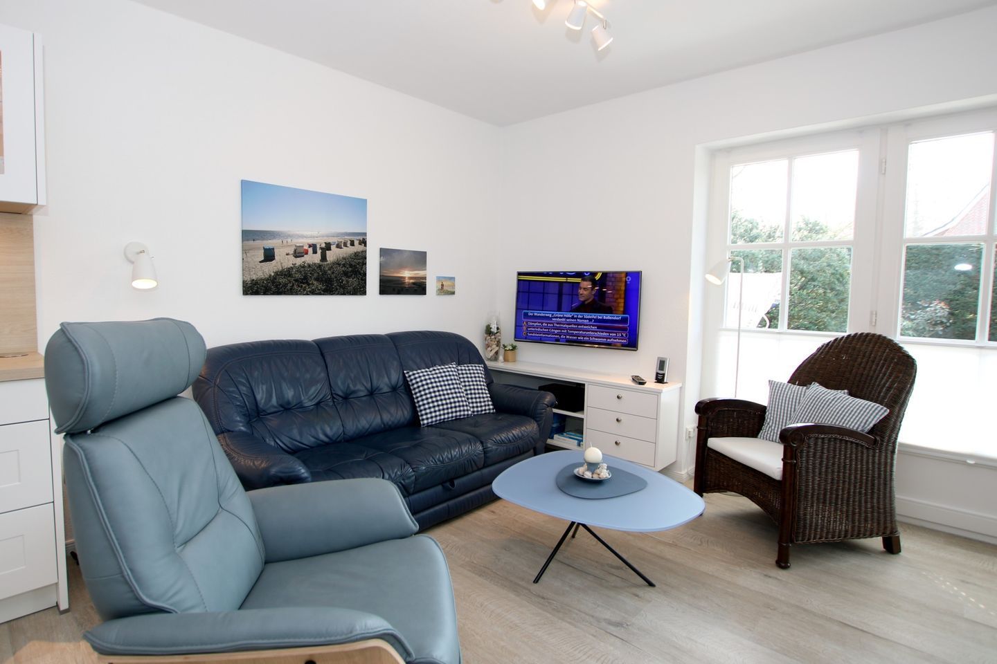 En moderne stue med sofa, lænestol og fletstol, et fjernsyn og et lille bord med en dekorativ genstand.