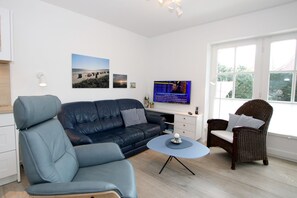 A modern living room with a sofa, armchair, and wicker chair, a television, and a small table with a decorative item.