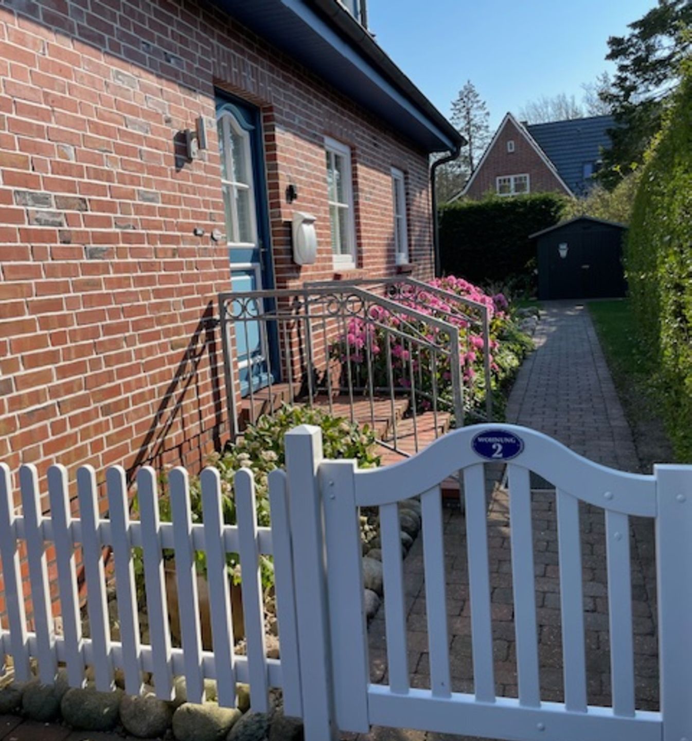 A brick house with a white picket fence, a pathway, and a sign indicating 'WORSTING 2'.