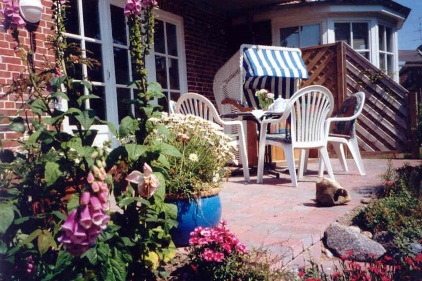 A patio with white plastic chairs, a table, and a blue and white striped umbrella.