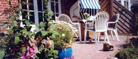 A patio with white plastic chairs, a table, and a blue and white striped umbrella.
