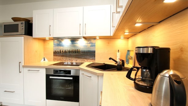 A compact kitchen with white cabinets, a microwave, an oven, a coffee maker, and a kettle. - Olhörnstieg 6, Whg. 2 Inselliebe - Apartment with 3 rooms on approx. 53m² (Wyk auf Föhr)