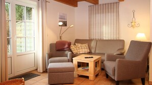 Un salon comprenant un canapé, deux fauteuils, une table basse et une fenêtre avec des stores.