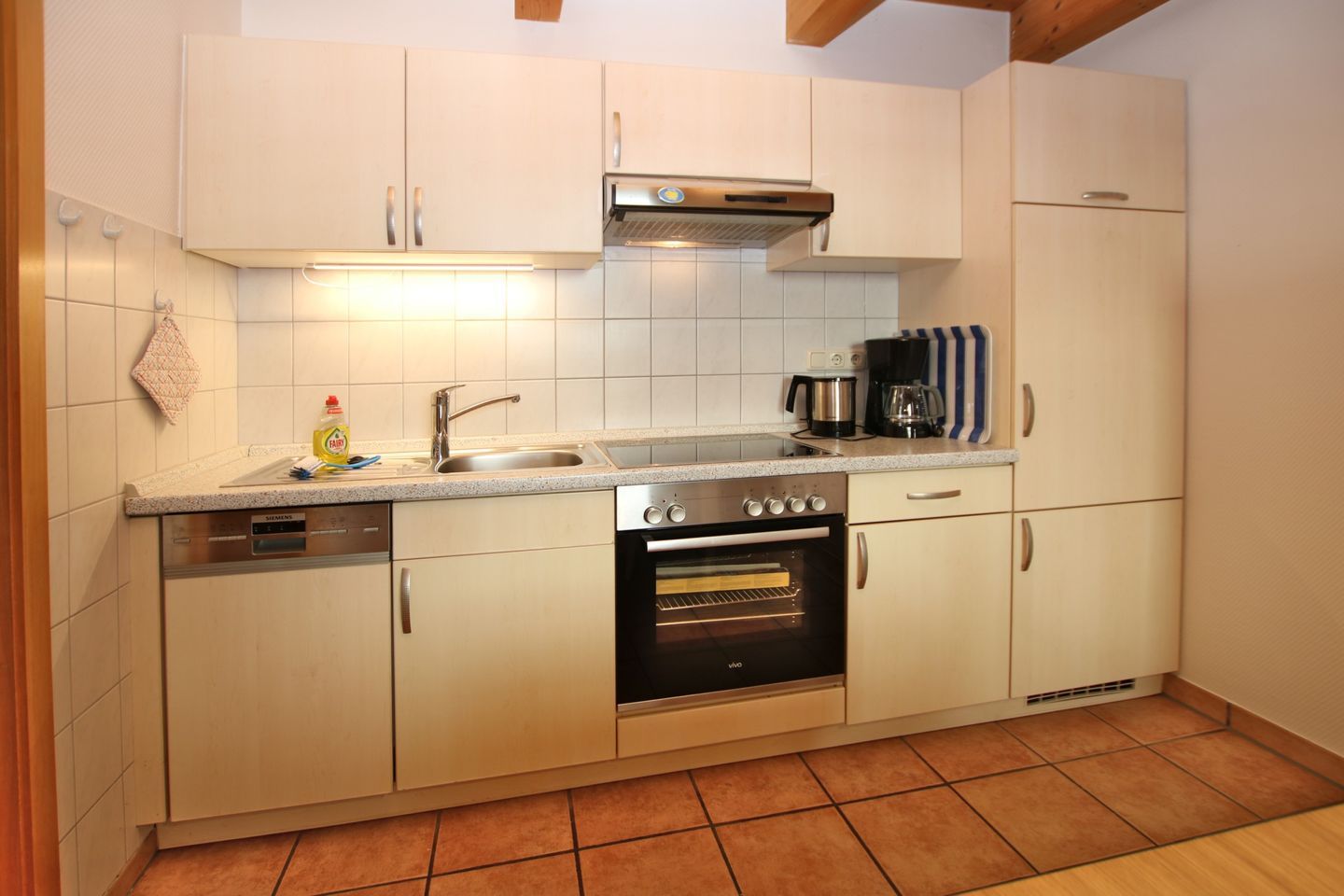 A compact kitchen with white cabinets, a stainless steel sink, a built-in oven, and a coffee maker.
