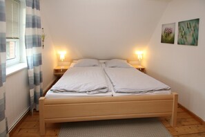 Una cama doble con dos mesitas de noche, una ventana con cortinas y dos lámparas de pared.