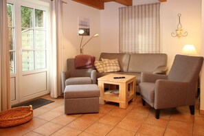 Una sala de estar con un sofá, dos sillones, una mesa de centro y una ventana con persianas.