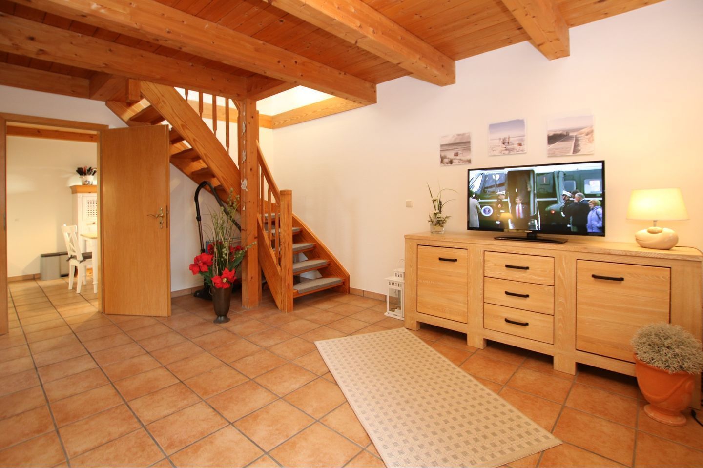 A spacious living room with a wooden staircase, a television, and a dining area with a chair and table.