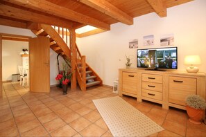 A spacious living room with a wooden staircase, a television, and a dining area with a chair and table. - Fehrstieg 1 c - Detached vacation home, approx. 75 m² and 3 rooms, large garden (Wyk auf Föhr)