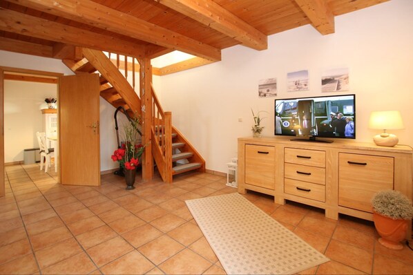 A spacious living room with a wooden staircase, a television, and a dining area with a chair and table.