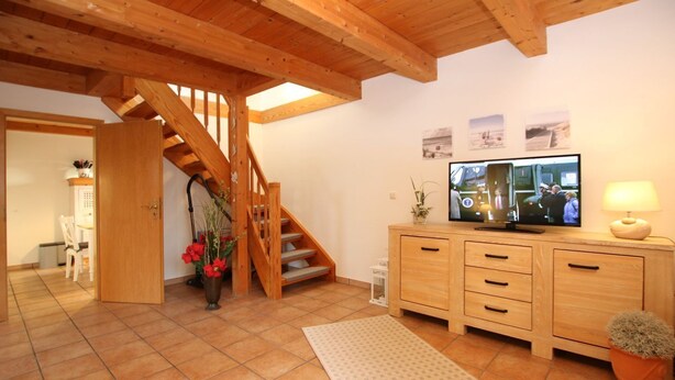 Un salon spacieux avec un escalier en bois, une télévision et un coin repas comprenant une chaise et une table.