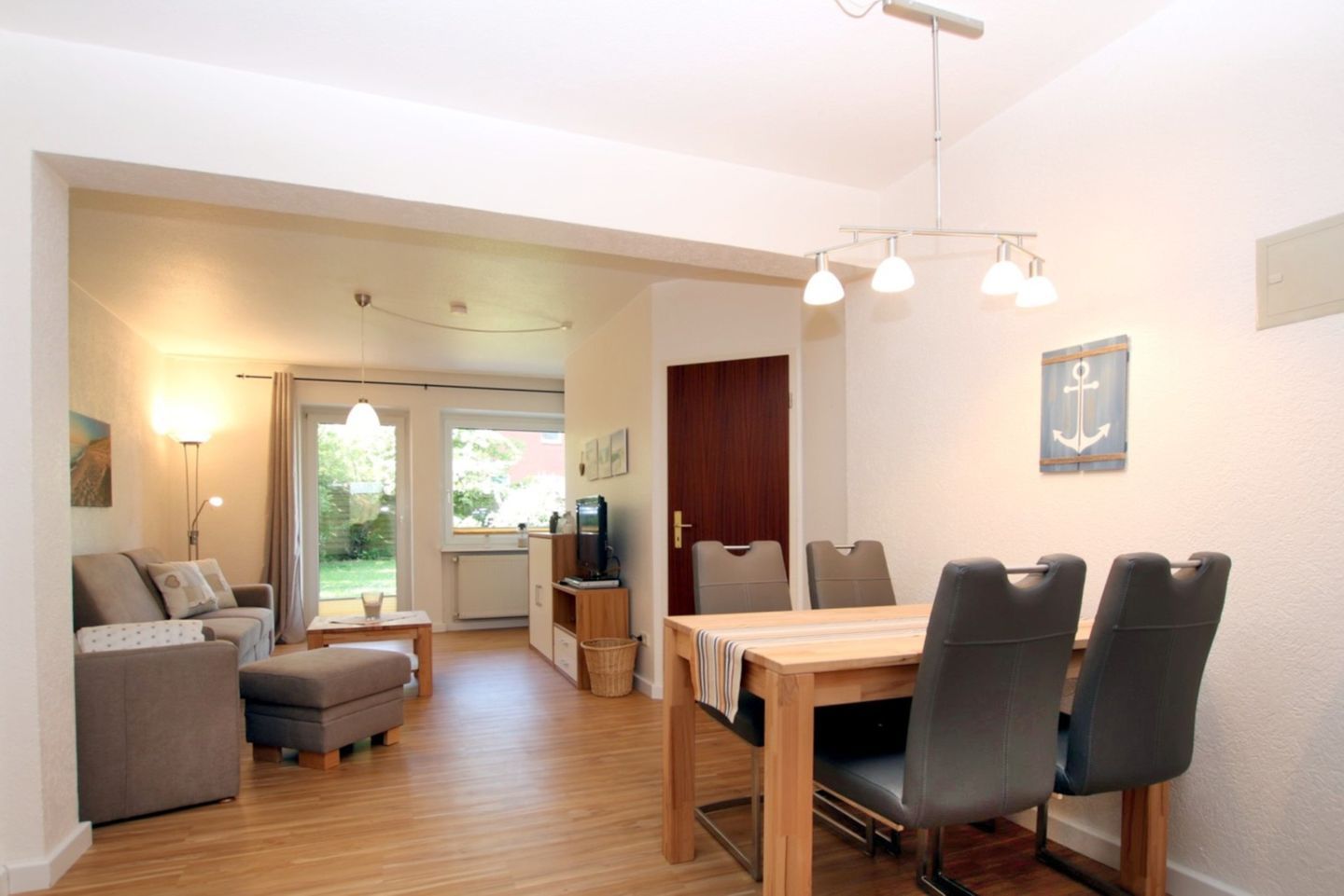 A room with a dining table, chairs, a sofa, a TV, and a window.