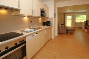 A compact kitchen with a stove, microwave, and sink, leading to a dining area with a sofa and table.
