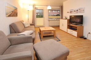 A modern living room with a sofa, coffee table, TV, and kitchen area.