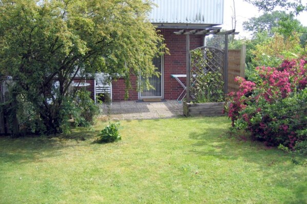 A brick building with a metal roof, a wooden fence, and a garden with grass and shrubs.