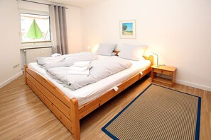 A single bed with a wooden frame, a bedside table with a lamp, a window with curtains, and a picture on the wall.