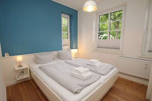 A bedroom with a large bed, two bedside tables, a window with blinds, and a ceiling light.
