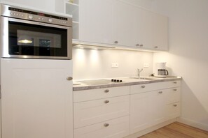 A modern kitchen with white cabinetry, a built-in oven, a sink, and a coffee maker.
