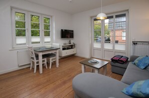 Una habitación con una mesa de comedor, sillas, un sofá, un televisor y ventanas amplias.