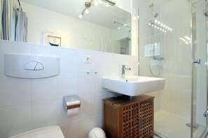 A modern bathroom with a white sink, a mirror, a shower, and a toilet. - Badestraße 18a, Whg. 1 - vacation apartment with 3 rooms, approx. 60m², in the center of Wyk, (Wyk auf Föhr)