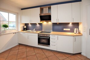 Una cocina moderna con armarios blancos, horno empotrado, estufa y una ventana con una planta.