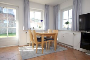 A dining area with a table and chairs, a television, and windows with curtains. - Badestraße 18a, Whg. 1 - vacation apartment with 3 rooms, approx. 60m², in the center of Wyk, (Wyk auf Föhr)