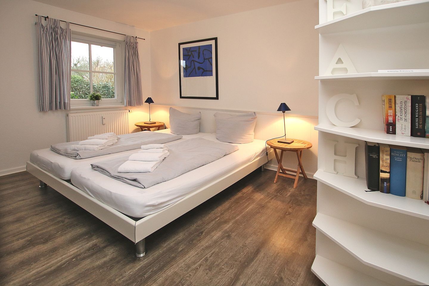 A bedroom with a bed, bedside tables, a bookshelf, and a window with curtains.