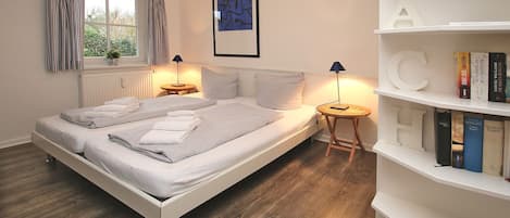 A bedroom with a bed, bedside tables, a bookshelf, and a window with curtains.