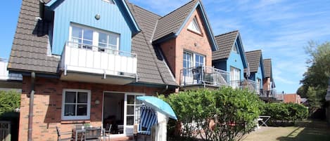 A row of two-story houses with a brick facade, blue trim, and a small front yard with a patio and a tree.