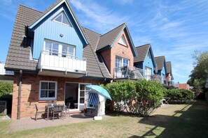 A row of two-story houses with a brick facade, blue trim, and a small front yard with a patio and a tree. - Badestraße 18a, Whg. 1 - vacation apartment with 3 rooms, approx. 60m², in the center of Wyk, (Wyk auf Föhr)