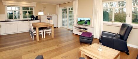 A spacious living area with a wooden dining table, a TV, and a leather sofa.