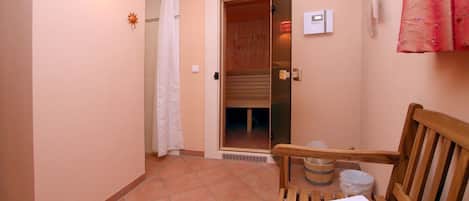 A bathroom with a shower, a bench with a towel, and a wall-mounted light fixture.