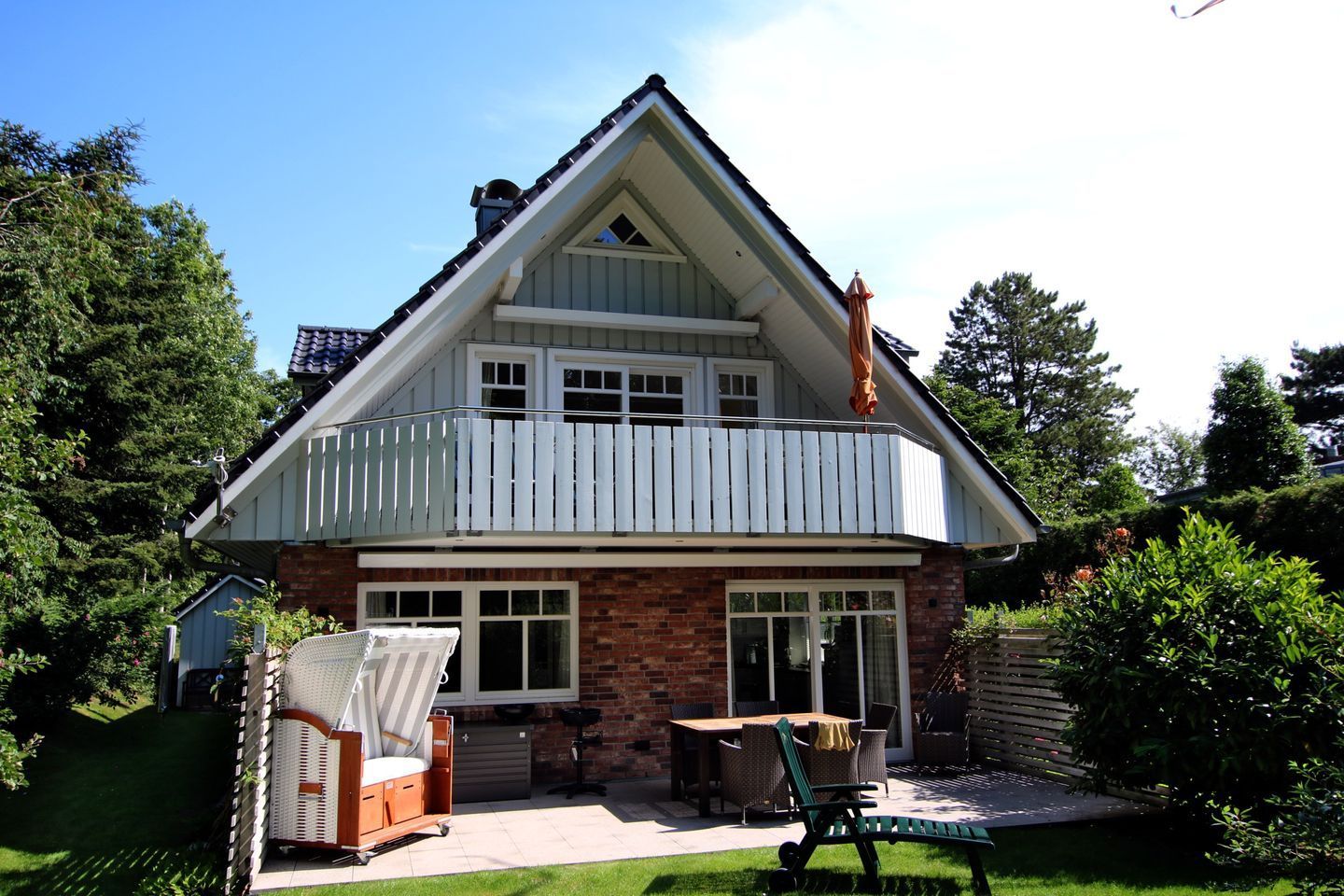 Une maison à deux étages avec un balcon, une terrasse dotée de mobilier d’extérieur et un abri de jardin dans le jardin.