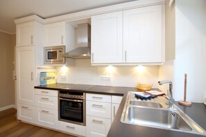 A modern kitchen with white cabinetry, stainless steel appliances, and a built-in oven.