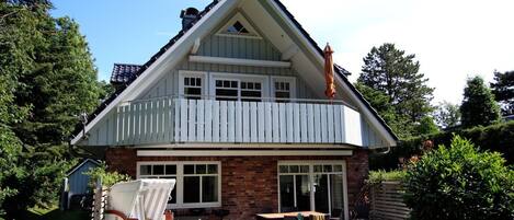 Une maison à deux étages avec un balcon, une terrasse dotée de mobilier d’extérieur et un abri de jardin dans le jardin.