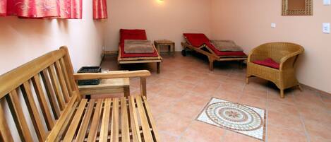 A room with a wooden bench, two lounge chairs, a small table, and a patterned floor.