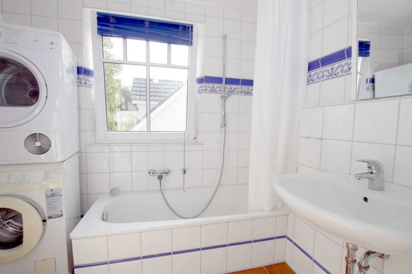 Une salle de bain équipée d’un lave-linge, d’une baignoire avec douche et d’un lavabo.