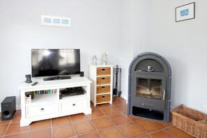 A living room with a flat-screen TV on a white entertainment unit, a grey fireplace, and a tiled floor. - Wiesenweg 4a, Whg. 3 - Ferienwohnung mit 3- Zimmern auf ca. 100m² (Wyk auf Föhr)