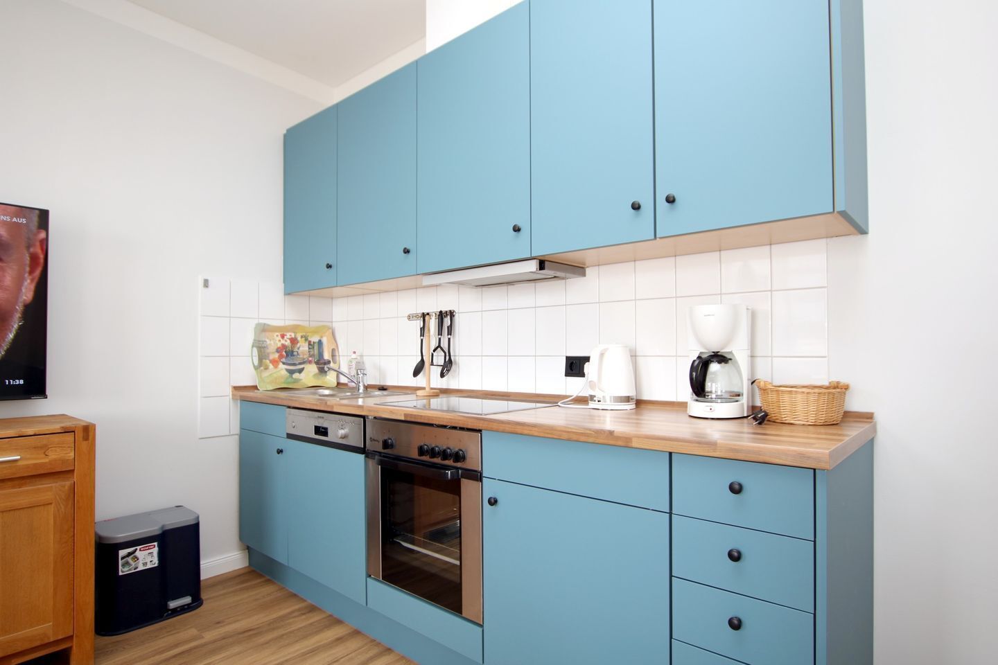 A modern kitchen with blue cabinets, a stainless steel oven, a coffee maker, and a trash bin.
