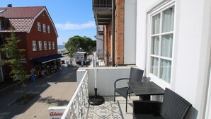 Een balkon met een tafel en stoelen, met uitzicht op een straat met winkels en een gebouw van rode baksteen.