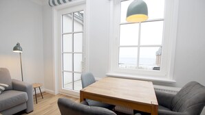 Een moderne woonkamer met een houten tafel, grijze banken, een klein rond tafeltje en een vloerlamp.