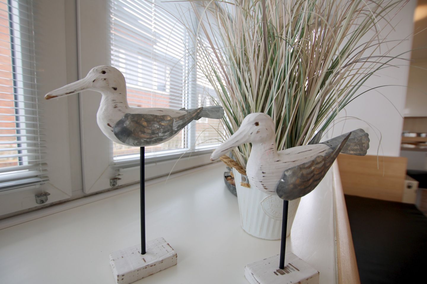 Two bird sculptures on stands near a window with blinds.